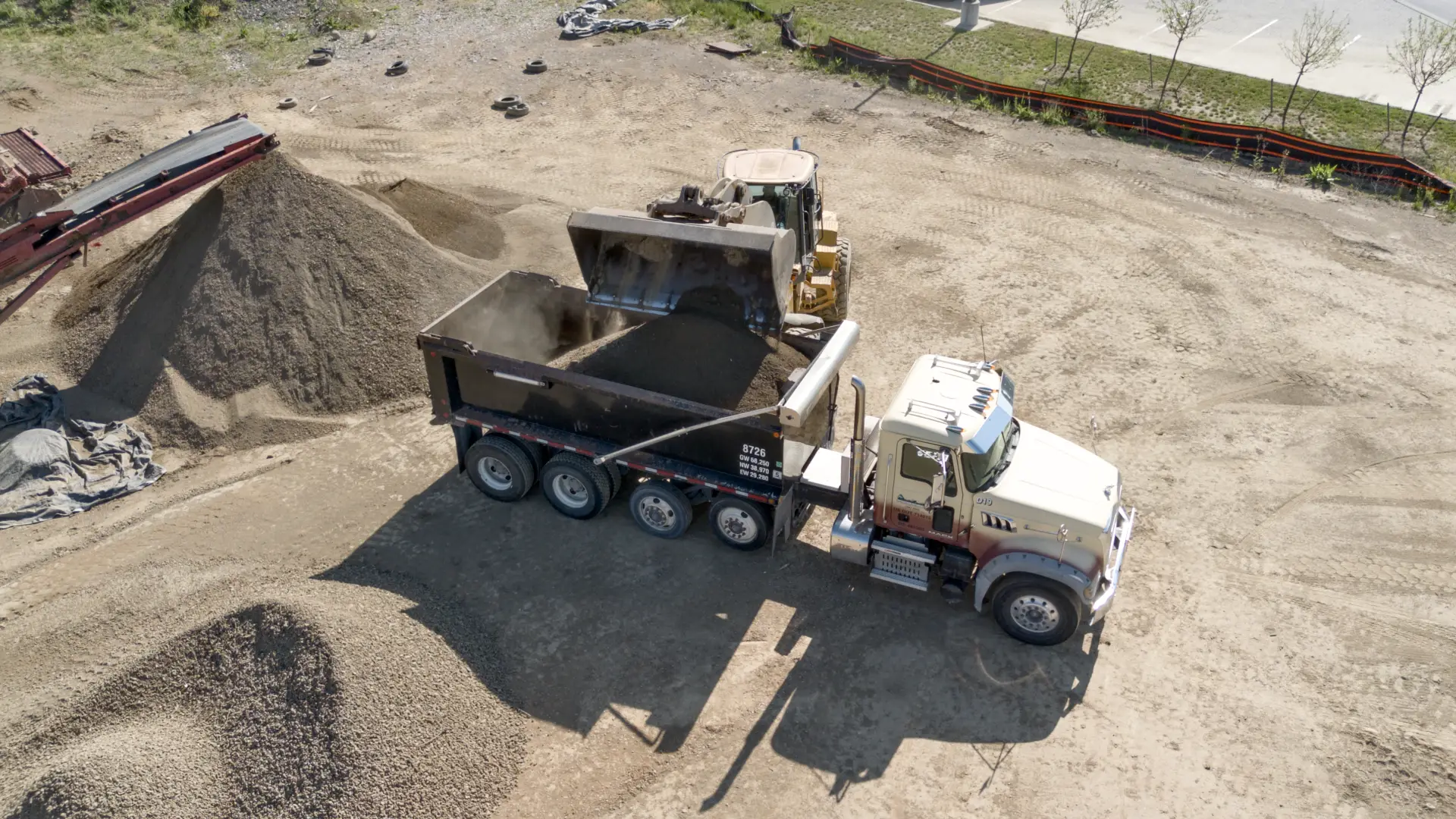 Dump truck being loaded by a wheel loader heavy hauling screened topsoil to a jobsite.